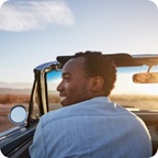 Man smiles and drives convertible into the sunset.